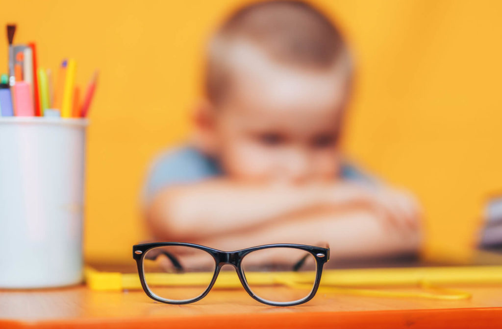 "Boy sitting in the background, unfocused, with glasses in sharp focus."