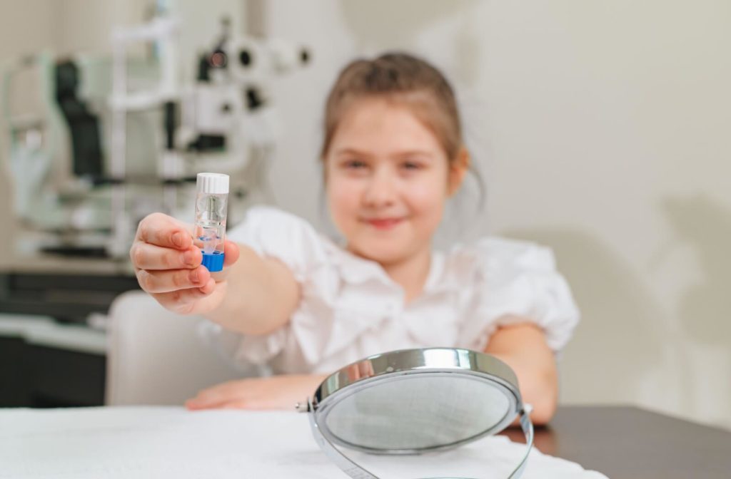 A young child in an optometrist’s eye exam room holds out a container of orthokeratological contact lenses