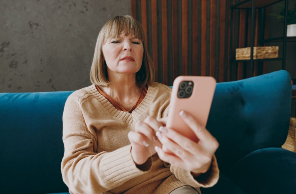 An older adult with myopia squints and holds their phone at a distance to see the screen clearly.