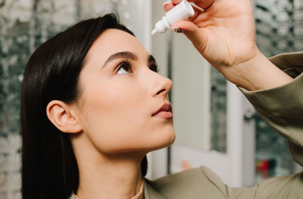 Young adult tilting their head back and applying eye drops from a small bottle to relieve dryness or irritation