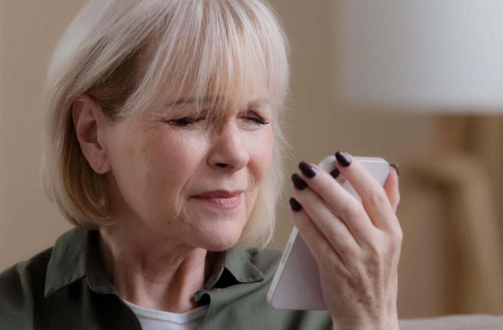 An older adult holding their phone close to their face and squinting due to worsening astigmatism.