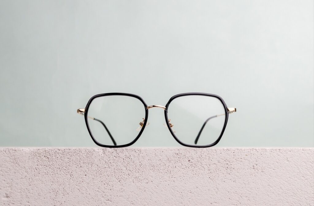 Thick-rimmed eyeglasses with a geometric shape sit on a stone wall.