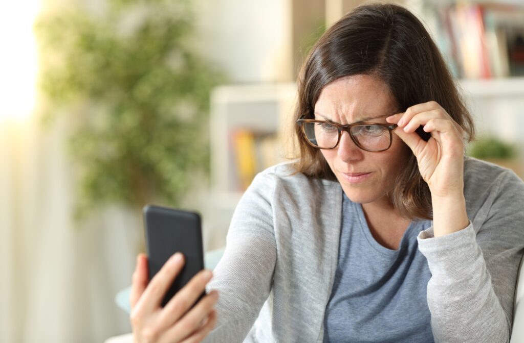 An adult wearing glasses and squinting at their phone.