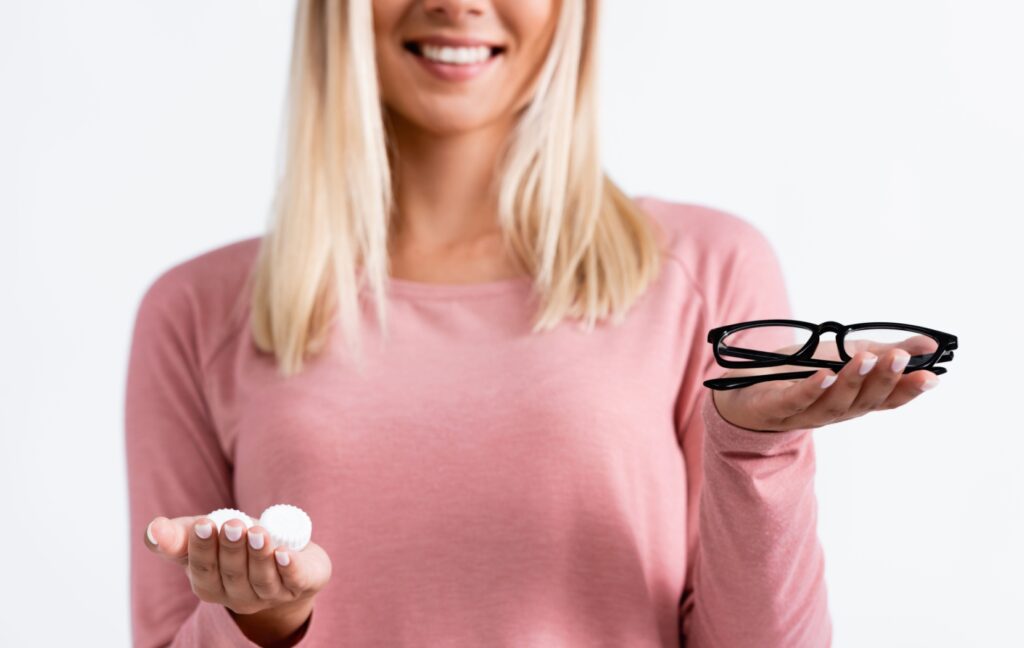 A person holds a pair of eyeglasses in one hand and contact lenses in the other hand. Both options are common solutions for myopia and hyperopia.