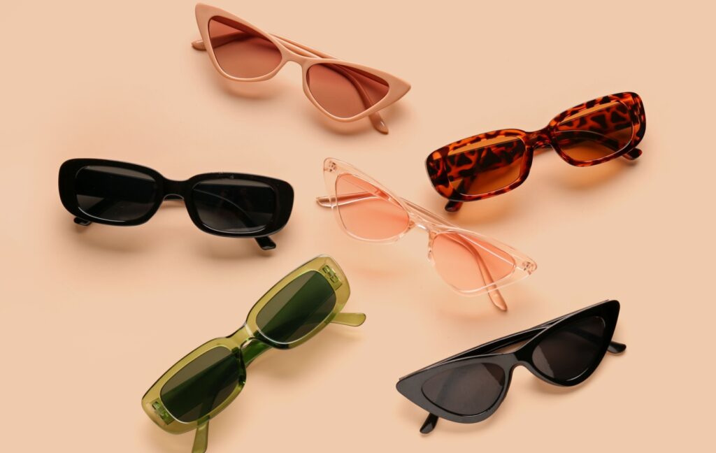 Several pairs of trendy sunglasses are arranged in a circle on a pink background.