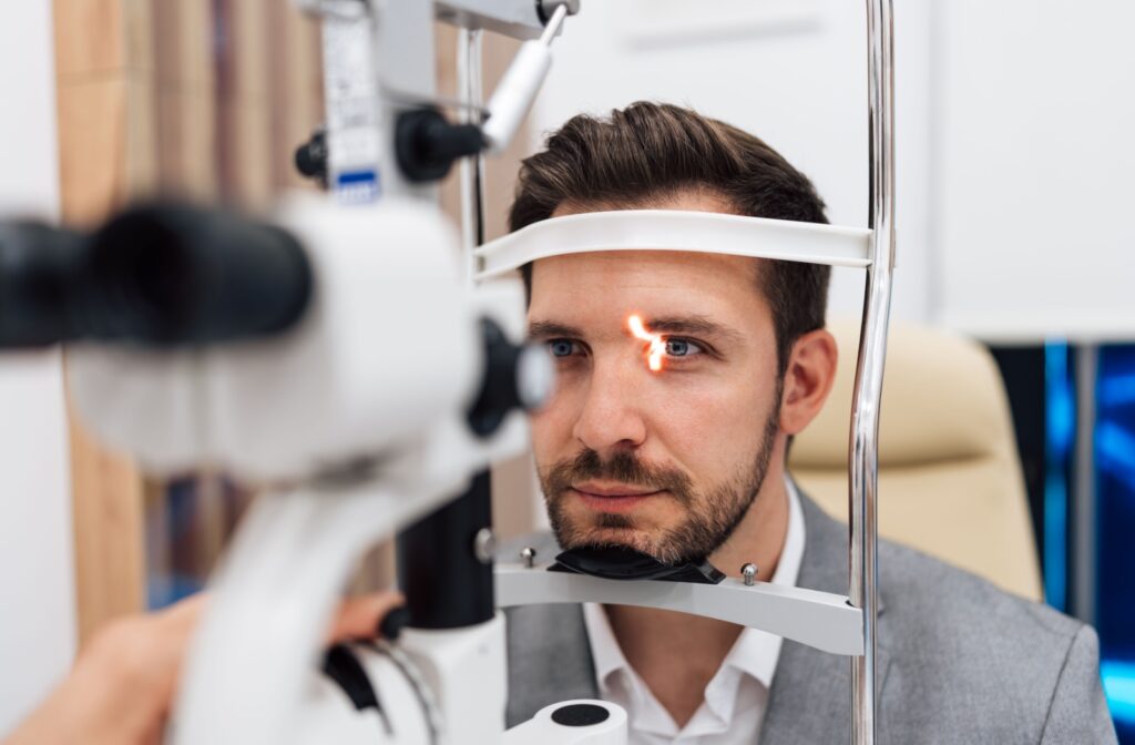 A person undergoes an eye exam using a slit-lamp machine, with a bright light focused on their eye.