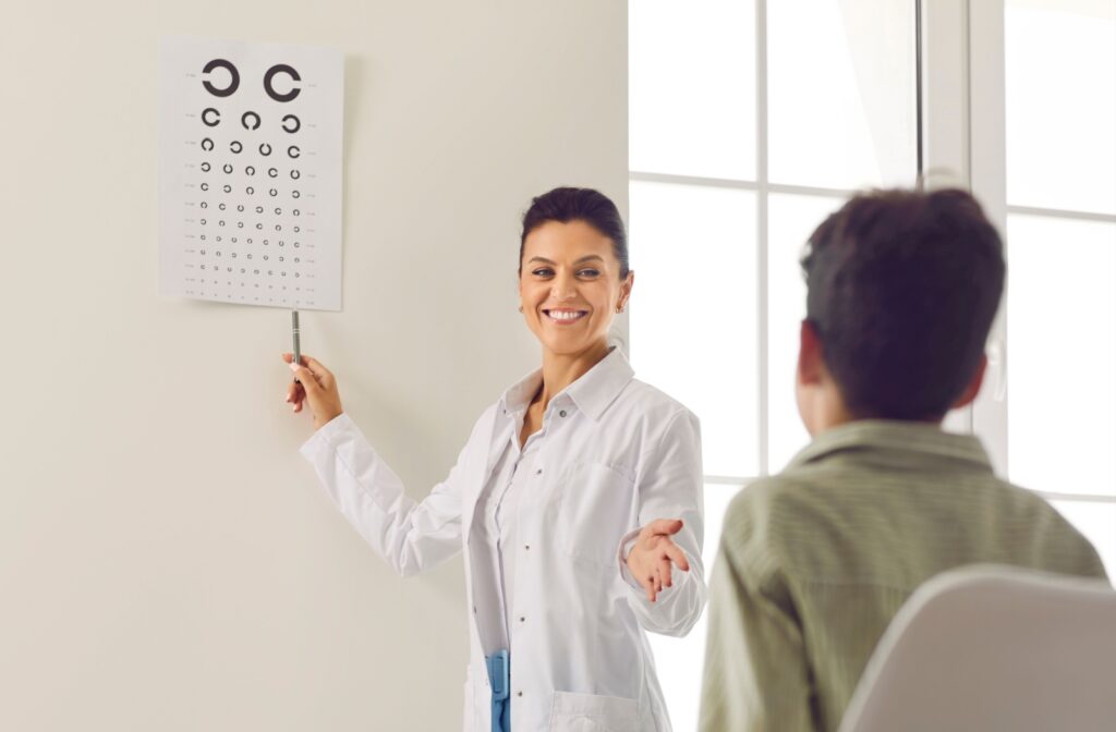 An eye doctor smiles while pointing to a vision chart as a patient sits in front of them.