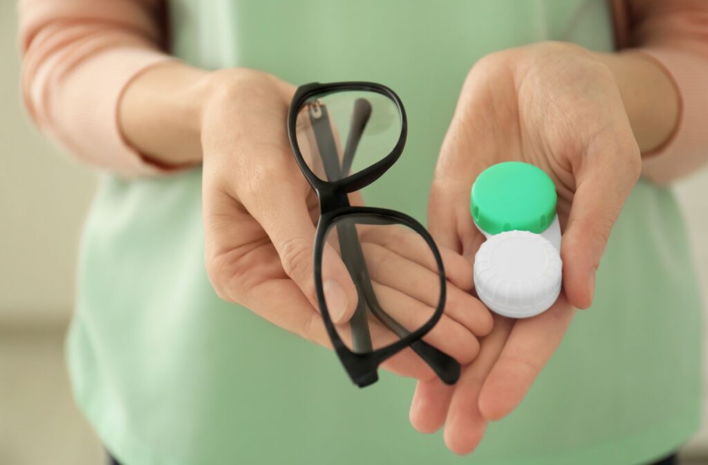 A pair of hands holding up glasses and contact lens case