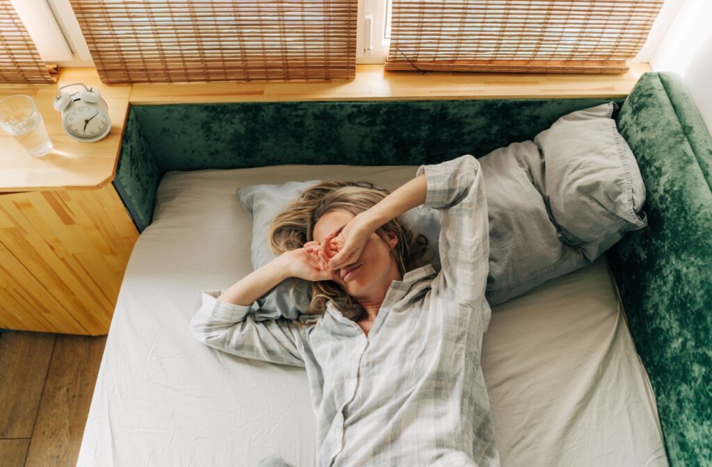 Woman rubs her eyes as she lays down in bed